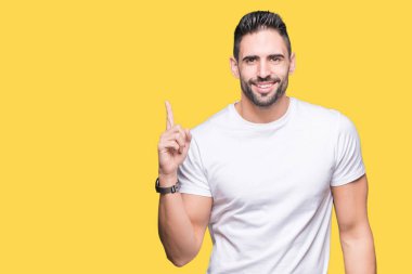Genç adam, yüzünde kocaman bir gülümseme ile izole arka plan üzerinde rahat beyaz t-shirt giyen kameraya bakarak yan el ve parmak ile işaret.