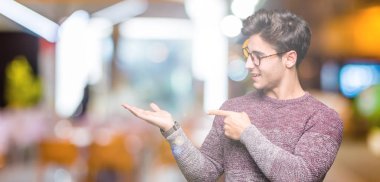 Hayret ve el ile sunulması ve parmak ile işaret ederken kameraya gülümseyen izole arka plan üzerinde gözlük takan genç yakışıklı adam.