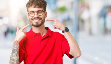 Kendinden emin gösterilen ve işaret parmakları diş ve ağız ile gülümseyen izole arka plan üzerinde gözlük takan yakışıklı delikanlı. Sağlık kavramı.