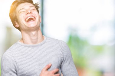 Genç yakışıklı adam giyen kış kazak izole üzerinde arka plan gülen ve komik deli şaka çünkü yüksek sesle zor gülüyor. Mutlu ifade.