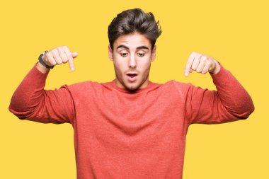 İzole genç yakışıklı adam arka plan işaretleme aşağı reklam, sürpriz yüz ve açık ağız gösterilen parmakları ile