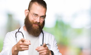 Mutlu ve komik yüz ile kamera parmaklar işaret tıbbi ceket giyen sakal ile genç sarışın doktor adam. İyi enerji ve Vibes.