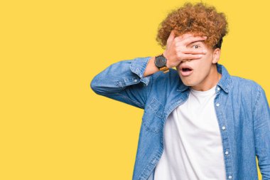 Mahcup ifadeyle parmaklarımın arasından seyir yakışıklı delikanlı afro saçlı kot ceket yüz ve gözler el ile kapsayan şok bakmak giyiyor.