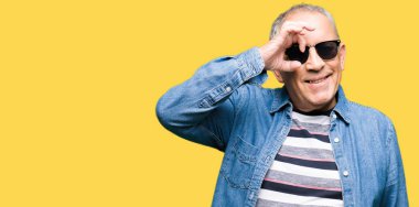 Parmakları ile mutlu yüz üzerinden seyir göz yakışıklı komuta sizde giyen denim ceket ve el gülümseyen, ok jest yapıyor güneş gözlüğü.