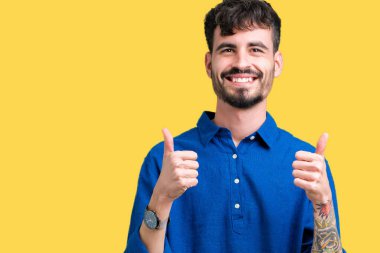 Yakışıklı delikanlı izole arka plan başarı işareti el ile pozitif jest yapıyor üzerinde başparmak gülümseyen ve mutlu. Neşeli bir ifadeyle, kazanan jest kameraya bakıyor.