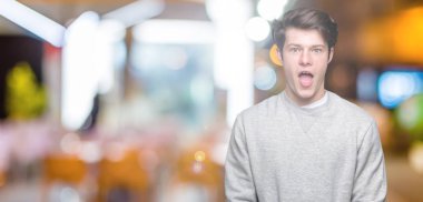 İzole arka plan korkuyor ve şok sürpriz ifade, korku ve heyecan yüz üzerinden sweatshirt giyen genç yakışıklı sportif adam.