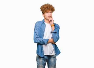 Yakışıklı genç afro saçlı çene düşünme hakkında soru, dalgın ifade üzerine el ile kot ceket giyiyor. Düşünceli yüzüyle gülümsüyor. Şüphe kavramı.