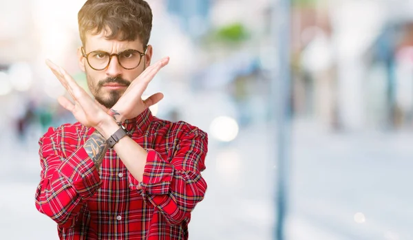 Young handsome man wearing glasses over isolated background Rejection expression crossing arms doing negative sign, angry face