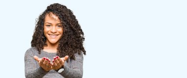 Kıvırcık saçlı gri kazak el avuç içi ile birlikte gülümseyen giyen genç güzel kadın alma veya jest vererek. Ayrı tutma ve koruma