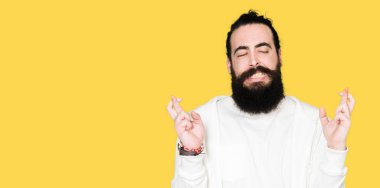 Uzun saç ve sakal geçiş parmakları umut ve gözler gülümseyen sportif sweatshirt giyen genç adamla kapalı. Şans ve batıl kavramı.