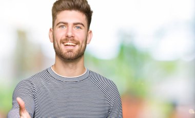 Genç yakışıklı adam çizgili kazak tebrik ve davetkar olarak dostu sunan el sıkışması gülümseyen giyiyor. Başarılı iş.