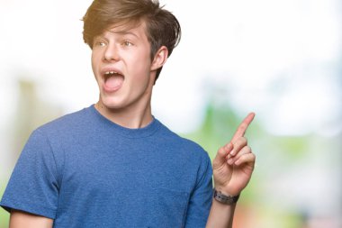 Genç yakışıklı adam yüzünde büyük bir gülümseme ile izole arka plan üzerinde mavi t-shirt giyen, kameraya bakarak yan el ve parmak ile işaret.