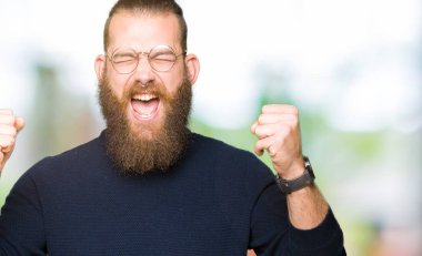 Gözlük ve balıkçı kazak giyen genç sarışın adam silah ile başarı için heyecanlı gülümsemek kutlamak yükseltilmiş kazandı. Kazanan kavramı.