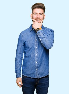 Emin çapraz kollar ve çeneme kaldırdı el ile gülümseme ile kameraya bakarak rahat kot gömlek giymiş genç yakışıklı sarışın adam. Pozitif düşünce.