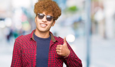 Yakışıklı genç afro saçlı hareketi el ile mutlu yaşasın yaparken güneş gözlüğü takıyor. Kameraya bakarak başarı gösteren ile ifade onaylama.