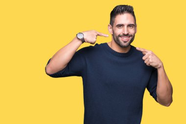 Genç yakışıklı adam kendinden emin gösterilen ve işaret parmakları diş ve ağız ile gülümseyen izole arka plan üzerinde kazak giyiyor. Sağlık kavramı.