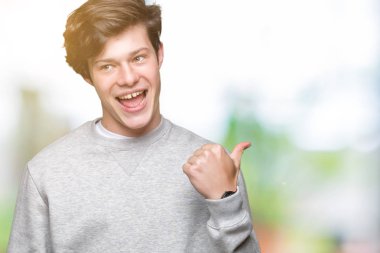 Seyir ve başparmak yanında yukarıyı mutlu yüz ile gülümseyen izole arka plan üzerinde sweatshirt giyen genç yakışıklı sportif adam.