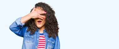 Mahcup ifadeyle parmaklarımın arasından arayan genç güzel kadın kıvırcık saçlı gözlüklü yüz ve gözler el ile kapsayan şok bakmak.