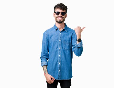 Yakışıklı delikanlı arıyor ve başparmak yanında yukarıyı mutlu yüz ile gülümseyen izole arka plan üzerinde güneş gözlüğü takıyor.