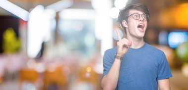 Başarılı fikirle izole arka plan işaret parmağı üzerinde gözlük takan yakışıklı delikanlı. Çıktıktan ve mutlu. Bir numara.