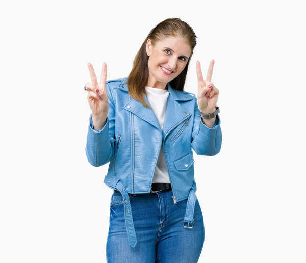 美しい中年熟女が笑みを浮かべて勝利のサインをやって指を表示するカメラを分離の背景にファッション革のジャケットを着てします — ストック写真