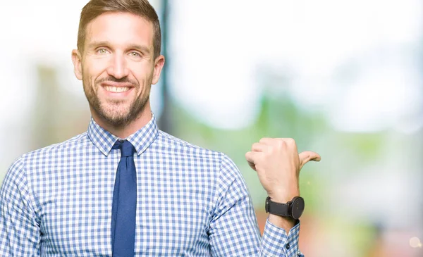 Handsome business man wearing tie smiling with happy face looking and pointing to the side with thumb up.