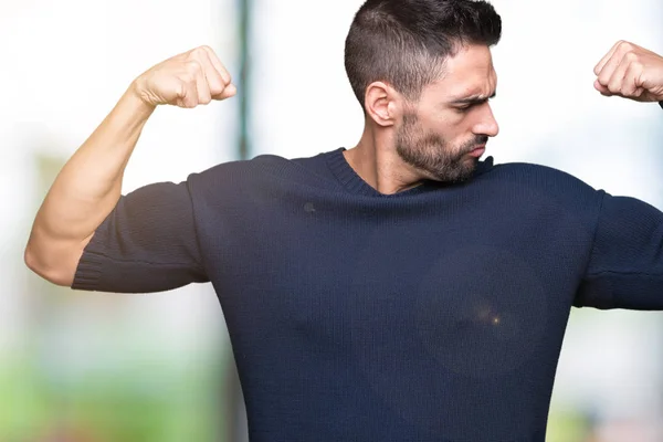 Young handsome man wearing sweater over isolated background showing arms muscles smiling proud. Fitness concept.