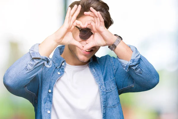年轻帅哥戴着太阳镜在孤立的背景做心脏形状与手和手指微笑通过标志 — 图库照片