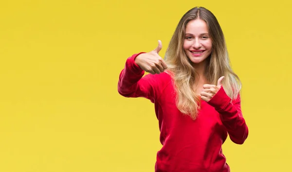 Young beautiful blonde woman wearing red sweater over isolated background approving doing positive gesture with hand, thumbs up smiling and happy for success. Looking at the camera, winner gesture.