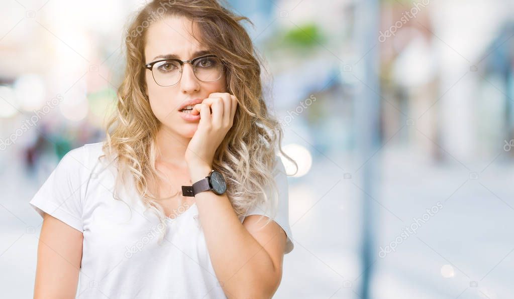 Beautiful young blonde woman wearing glasses over isolated background looking stressed and nervous with hands on mouth biting nails. Anxiety problem.