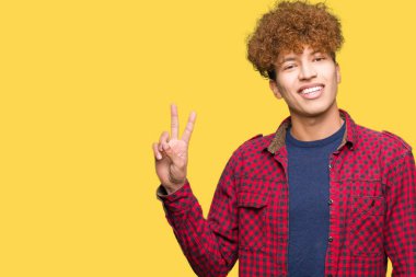 Afro saçlı Genç yakışıklı öğrenci adam zafer işareti yapıyor kamera mutlu yüz göz kırpıyor ile gülümseyen bir ceket giyiyor. İki numara.