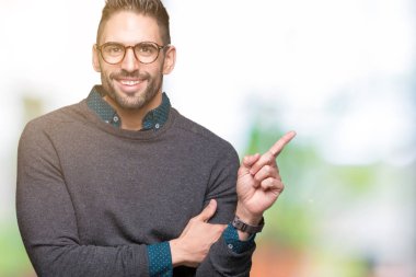 Kameraya bakarak yan el ve parmak ile işaret yüzünde kocaman bir gülümseme ile izole arka plan üzerinde gözlük takan genç yakışıklı adam.