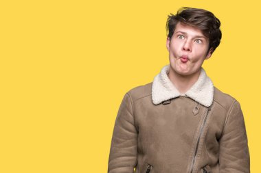 Genç yakışıklı adam dudaklar, deli ve komik jest ile balık yüz yapma izole arka plan üzerinde kış ceket giyiyor. Komik ifade.