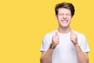 Zafer kutluyor gülümseyen izole arka kolları olan başarı için heyecan üzerinde rahat beyaz t-shirt giyen genç yakışıklı adam kaldırdı. Kazanan kavramı.