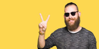 Genç hipster adam mutlu yüz zafer işareti yaparken kameraya göz kırpıyor ile gülümseyen güneş gözlüğü takıyor. İki numaralı.