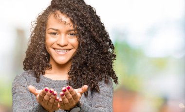 Kıvırcık saçlı gri kazak el avuç içi ile birlikte gülümseyen giyen genç güzel kadın alma veya jest vererek. Ayrı tutma ve koruma