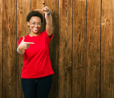 Elle yapma çerçeve ve parmakları ile mutlu yüz gülümseyen izole arka plan üzerinde gözlük güzel genç Afro-Amerikan kadın. Yaratıcılık ve Fotoğrafçılık kavramı.