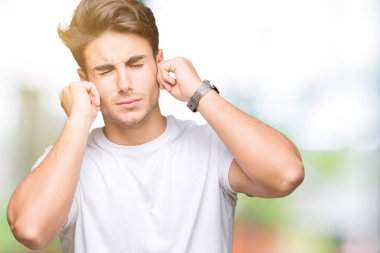 Yüksek sesle müzik gürültü rahatsız ifade parmaklarıyla kulaklarıyla kapsayan izole arka plan üzerinde beyaz t-shirt giyen genç yakışıklı adam. Sağır kavramı.