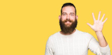 Kış kazak gösterme ve parmakları ile işaret giyen genç hipster adam kendinden emin ve mutlu gülümseyerek süre beş numara.