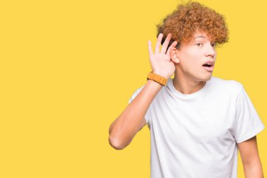 Afro saç ile genç yakışıklı adam rahat beyaz t-shirt kulağınıza söylenti ya da dedikodu bir işitme dinlerken el ile gülümsüyor giyiyor. Sağırlık konsepti.