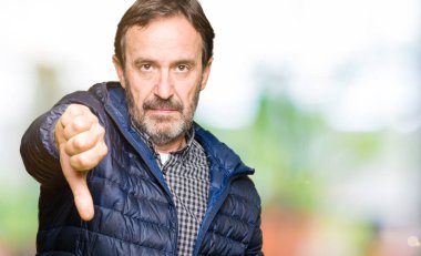 Orta yaş yakışıklı adam mutsuz ve kızgın ret gösterilen ve başparmak aşağı hareketi ile negatif seyir kış palto giyiyor. Kötü ifade.