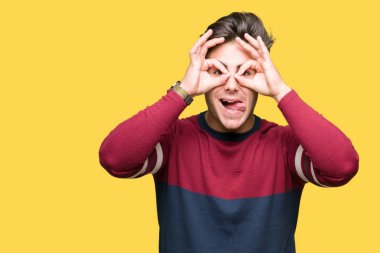 Yakışıklı delikanlı, dilini parmaklarının arasından baktığını yapışmasını dürbün gibi ok jest yapıyor izole arka plan üzerinde. Deli ifade.