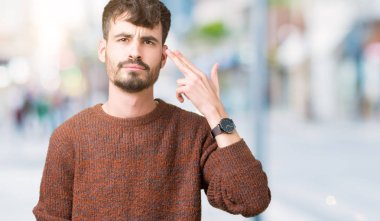 Genç yakışıklı adam giyen kış kazak izole üzerinde çekim ve öldürmek kendini el ve parmaklara baş, intihar jest işaret arka plan.