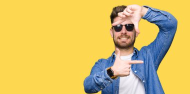 Elle yapma çerçeve ve parmakları ile mutlu yüz gülümseyen denim ceket giyen genç yakışıklı zarif adam. Yaratıcılık ve Fotoğrafçılık kavramı.