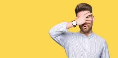 Şoka girmiş genç yakışıklı bir adam elleriyle yüzünü ve gözlerini kapatıyor, utanmış bir ifadeyle parmaklarından bakıyor..