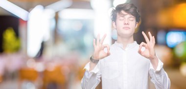 Genç yakışıklı iş adamı izole arka plan üzerinde dinlenmek ve gülümseyen gözlerle kapalı parmak jestle meditasyon yapıyor. Yoga kavramı.