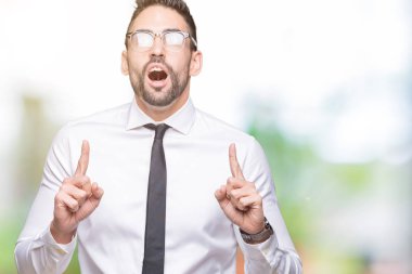 Genç yakışıklı iş adamı izole arka plan üzerinde gözlük hayret ve yukarıya bakıp parmakları ile işaret şaşırttı ve silah kaldırdı.