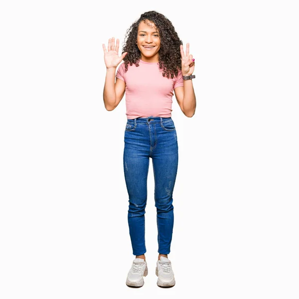 ピンクの シャツを着たカーリーヘアの若い美しい女性は 自信を持って幸せに笑っている間 指の数7を示しています — ストック写真