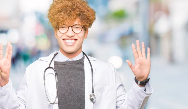 年轻英俊的医生男子穿着医疗外套显示和手指指向八号 而微笑着自信和快乐 — 图库照片