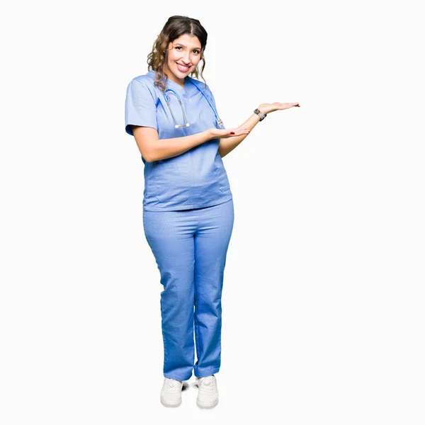 広告笑顔幸せと自信を持って提示手と開いた手のひら側に医療の均一なポインティングを着ている若い大人医師女性 — ストック写真